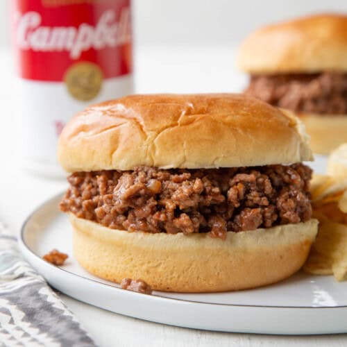 ground beef sloppy joe on a brioche bun, with a can of tomato soup in the background.