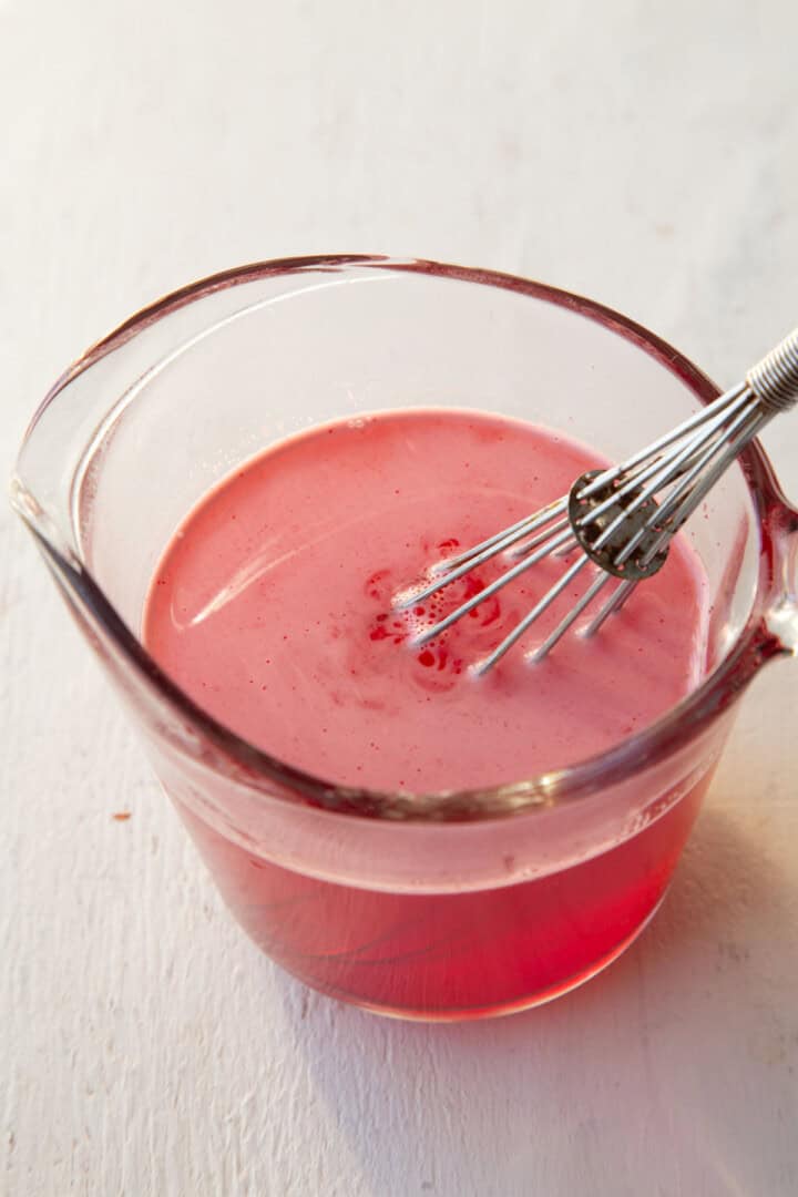 strawberry gelatin dissolved into water in a measuring cup.