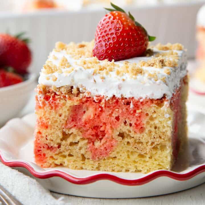yellow cake with strawberry jello poking through, topped with whipped topping, graham cracker crumbs, and a strawberry.