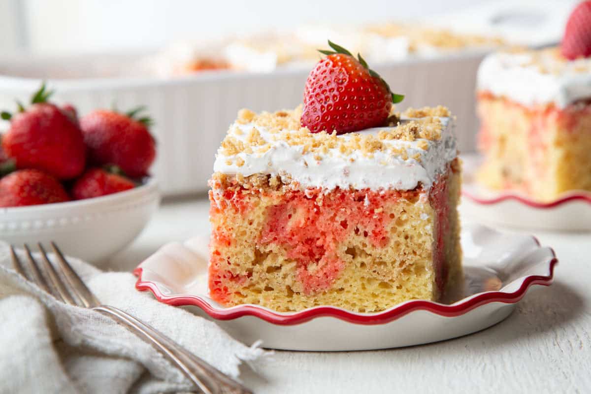 slice of poke cake with graham cracker crumbs, whipped topping, and a strawberry on top.