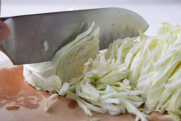 a knife thinly shredding cabbage.
