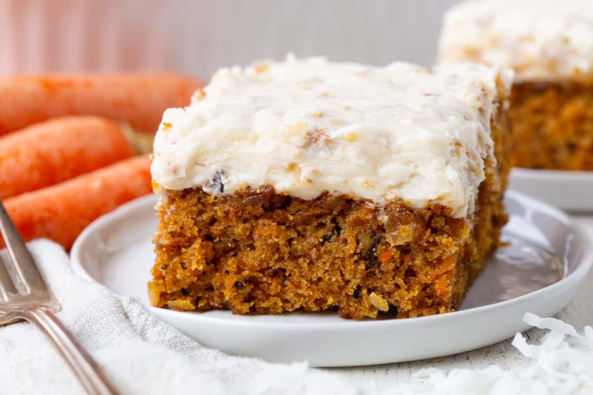 square slice of carrot cake with a coconut cream cheese frosting spread on top.