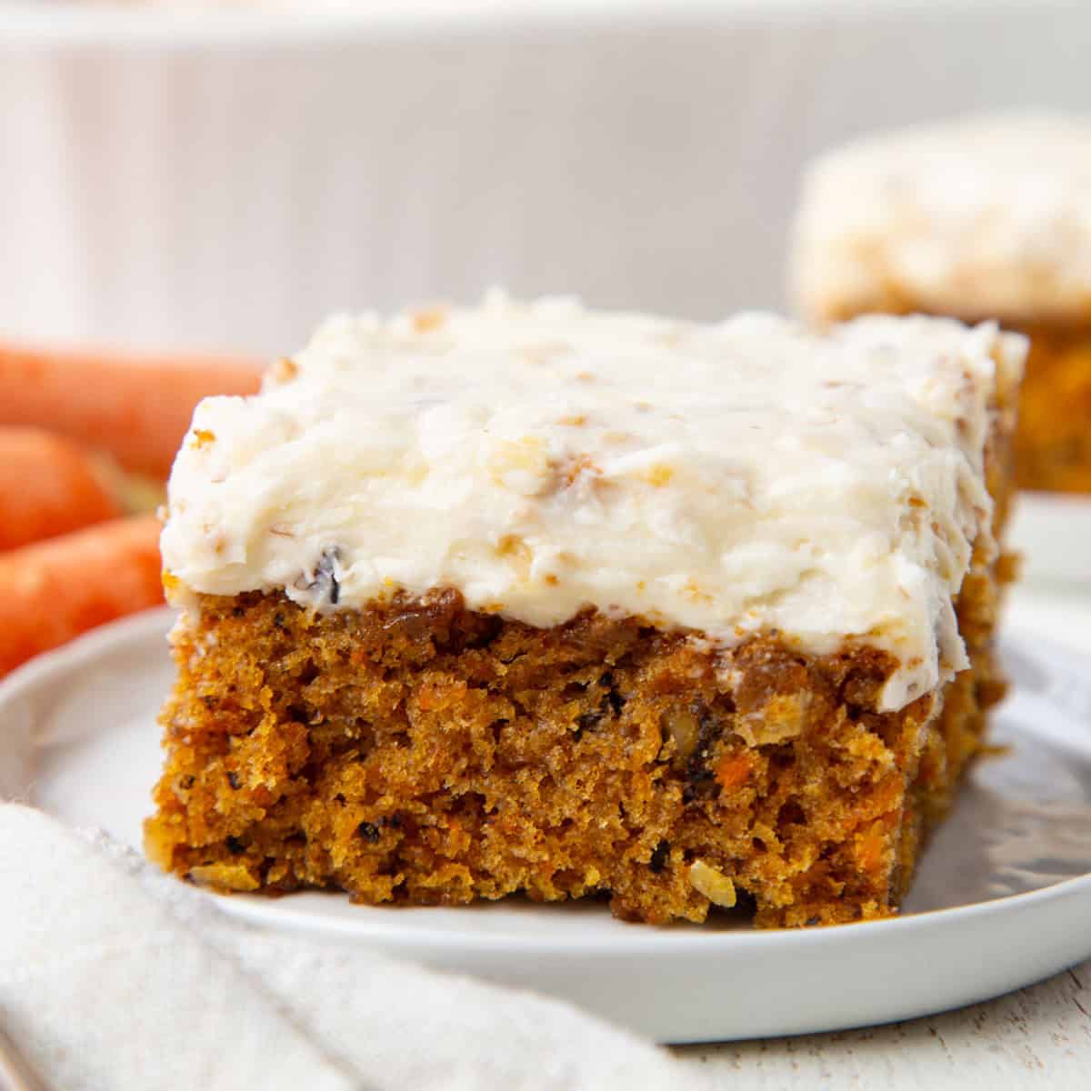 slice of carrot cake with a thick white cream cheese frosting with coconut inside on top.