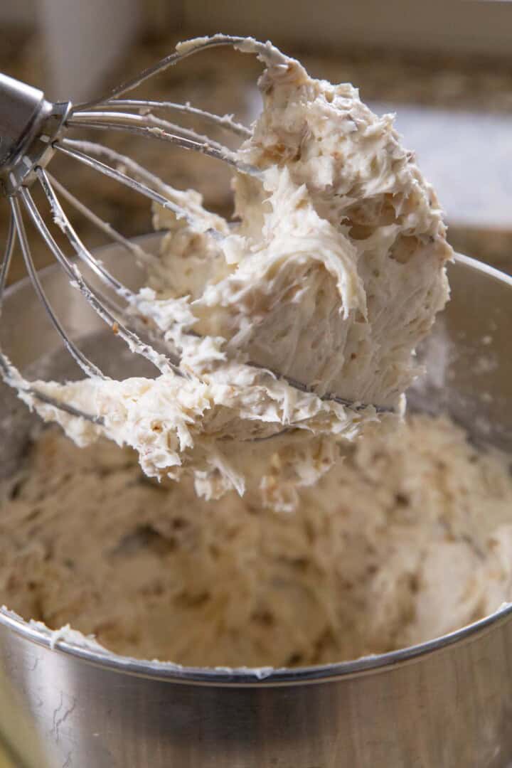 chunky cream cheese frosting with coconut in it, on the beater of a stand mixer.