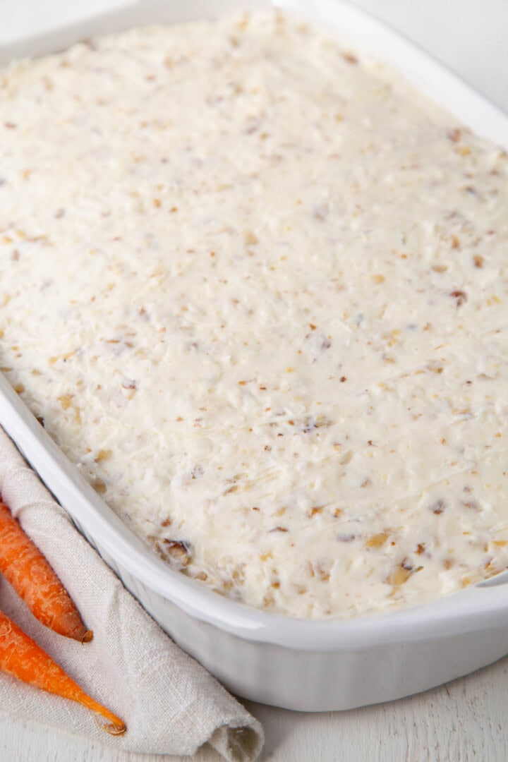 cake frosted with a white coconut cream cheese frosting in a white baking dish.