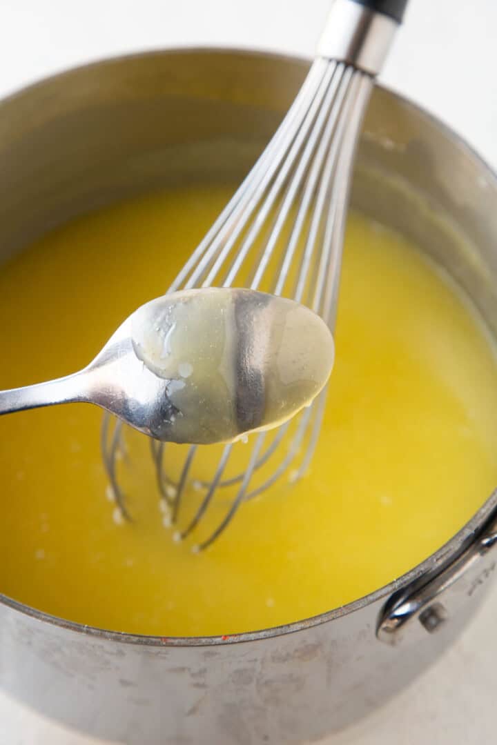 yellow mixture in a saucepan in the background with a spoon with a finger print through the yellow mixture on it.
