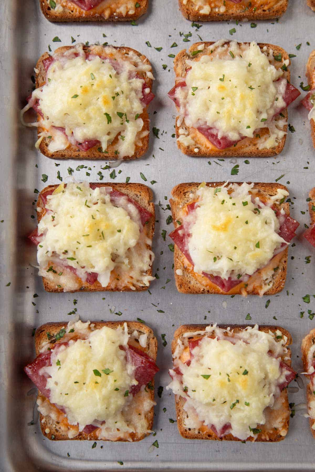 mini reuben sandwiches with squares of rye bread topped with corned beef and melted swiss cheese on a sheet pan.