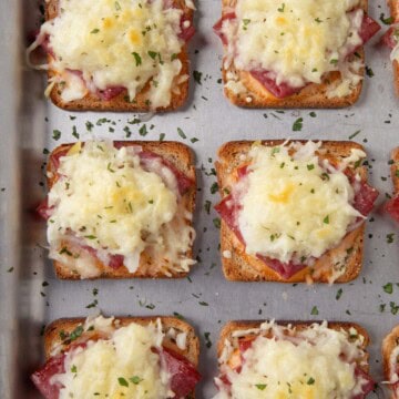 mini reuben sandwiches with a square of toasted rye bread topped with corned beef and melted swiss cheese on a sheet pan.
