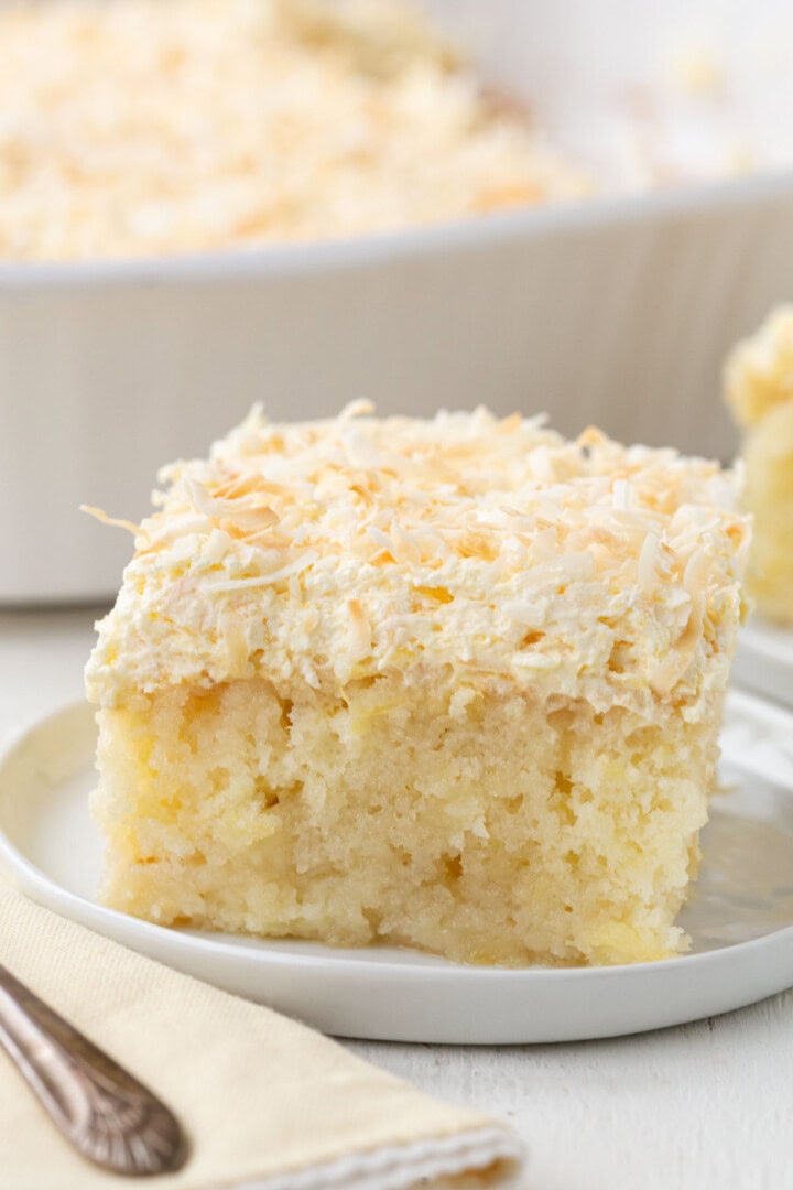 slice of yellow cake with bits of pineapple inside, topped with a fluffy frosting and toasted coconut.