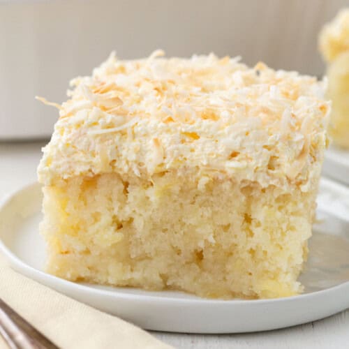 slice of yellow cake topped with toasted coconut on a white plate.