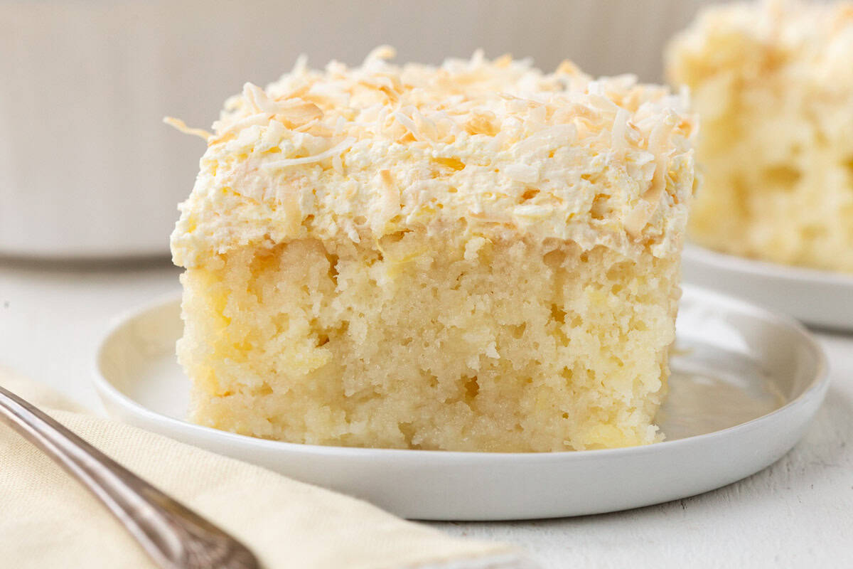 slice of yellow cake with bits of pineapple inside, topped with a fluffy frosting and toasted coconut.