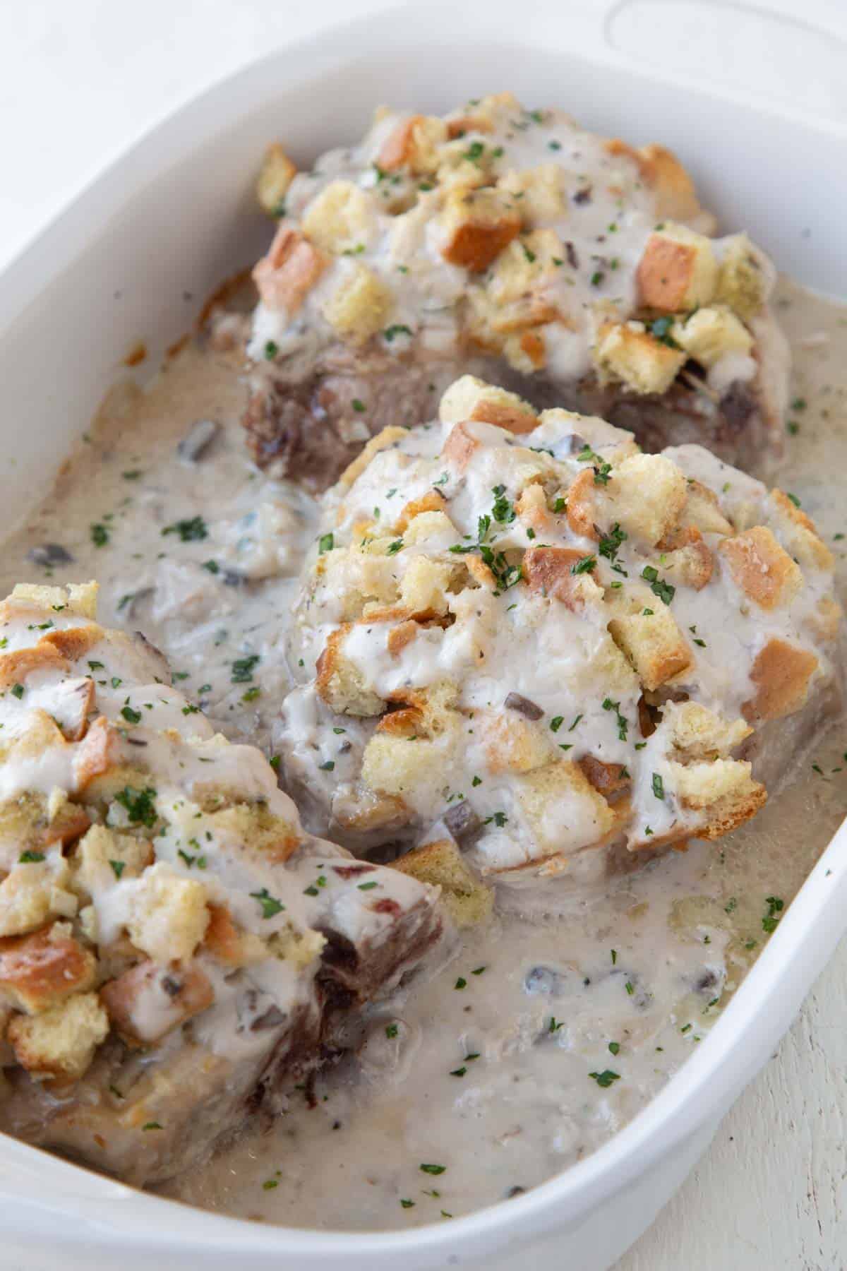 pork chops topped with stuffing and cream of mushroom soup in a baking dish.