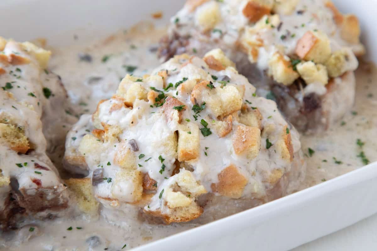 pork chops and stuffing with cream of mushroom soup in a baking dish, topped with parsley.