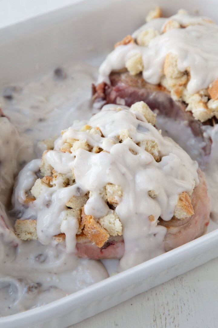 cream of mushroom soup on top of stuffing topped pork chops in a baking dish.