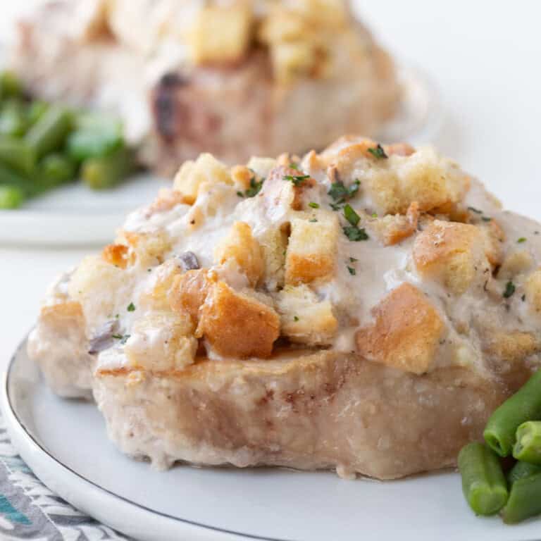 pork chop topped with stuffing and a creamy mushroom sauce on a white plate.