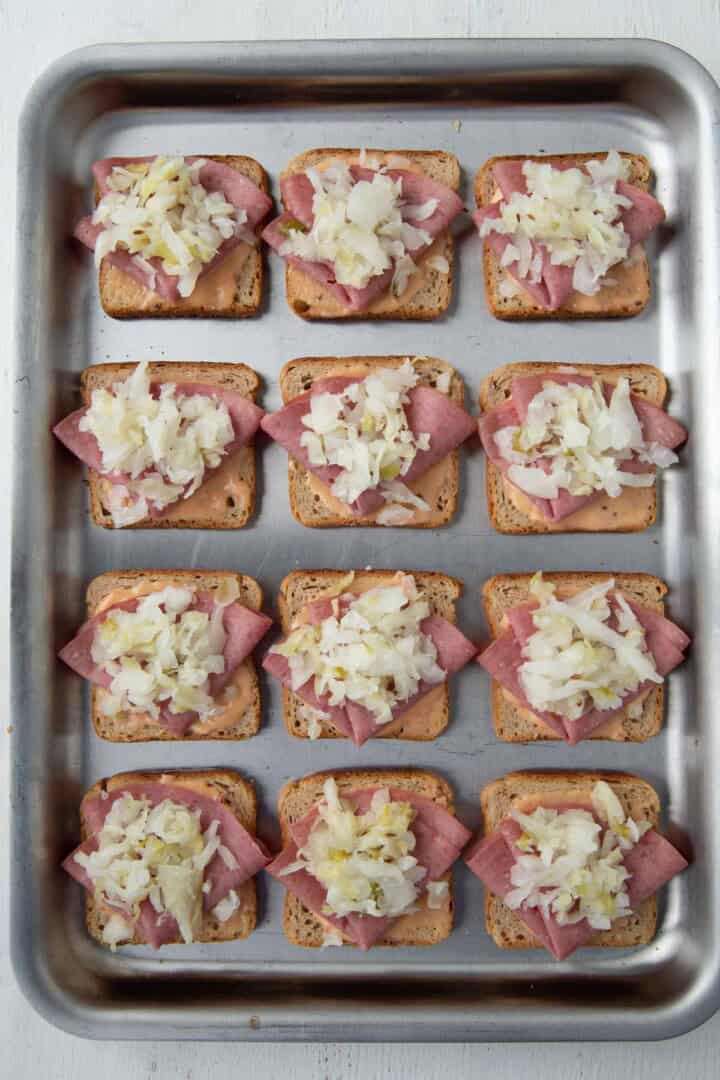rye bread squares topped with thousand island dressing, slices of corned beef, and sauerkraut.