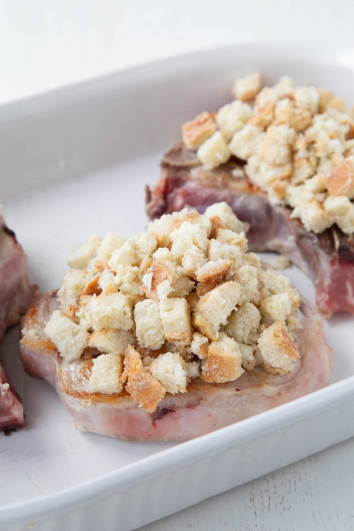 bread cubes on top of pork chops in a baking dish.