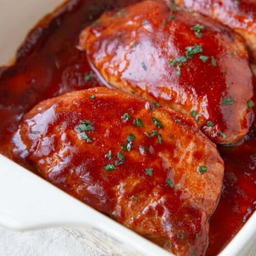 pork chops covered in bbq sauce in a baking dish.