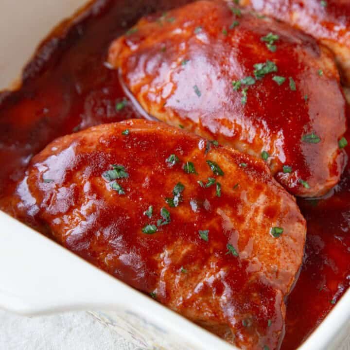 pork chops covered in bbq sauce in a baking dish.