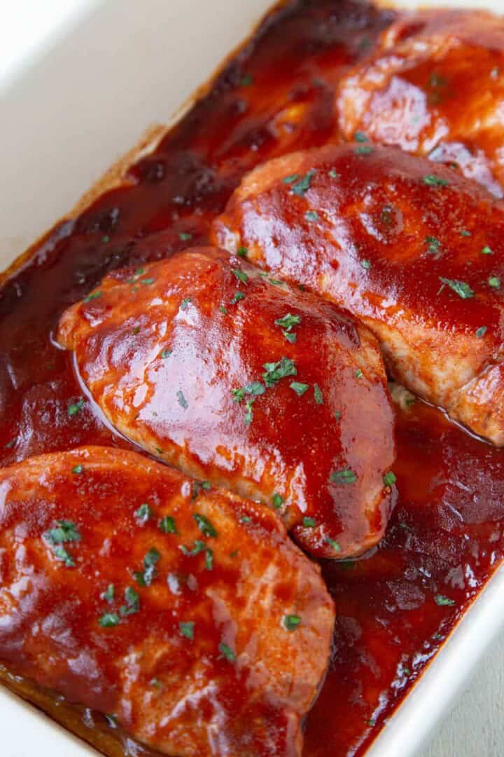 baked pork chops in a dish with bbq sauce over the top.