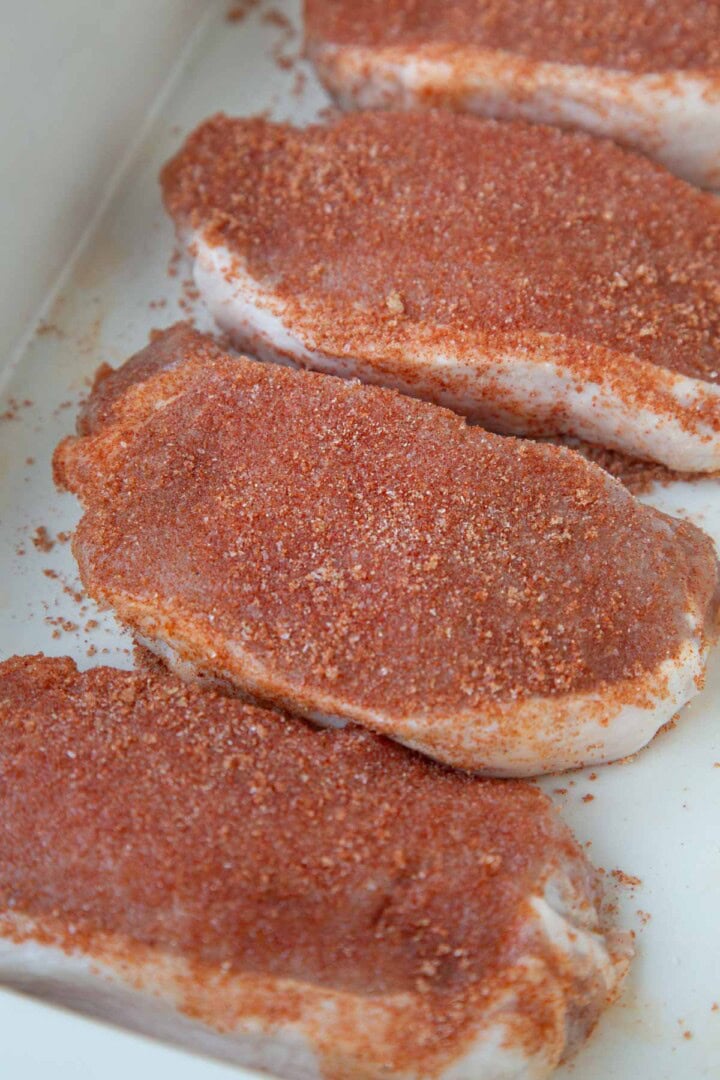 boneless pork chops in a baking dish with a bbq rub on them.