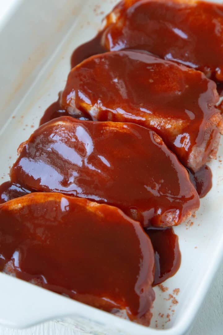 bbq sauce on top of pork chops in a baking dish.