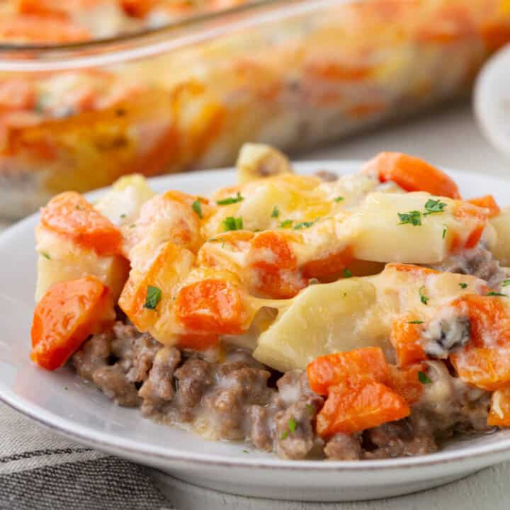 a scoop of a creamy casserole including ground beef in a creamy sauce, topped with chopped potatoes and chopped carrots, and cheese on top.