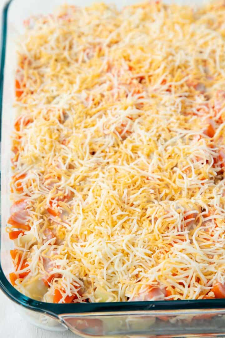 cheese on top of carrots and potatoes in a casserole dish.