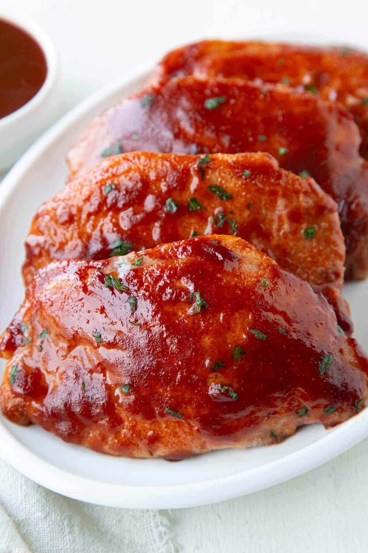 pork chops with bbq sauce on top on a white platter.