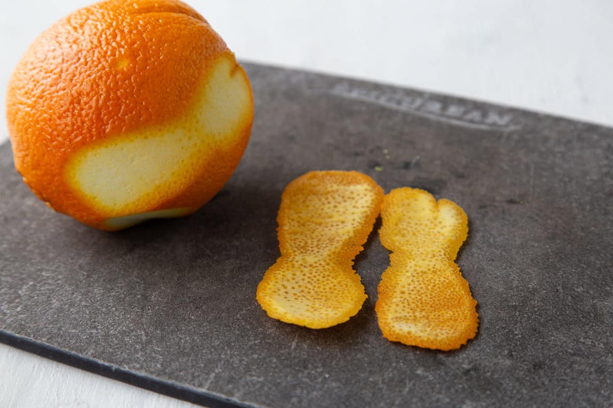 orange peel and a navel orange on a cutting board.