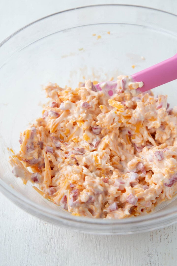 shredded cheddar and chopped pimentos in a creamy mayonnaise sauce in a mixing bowl.