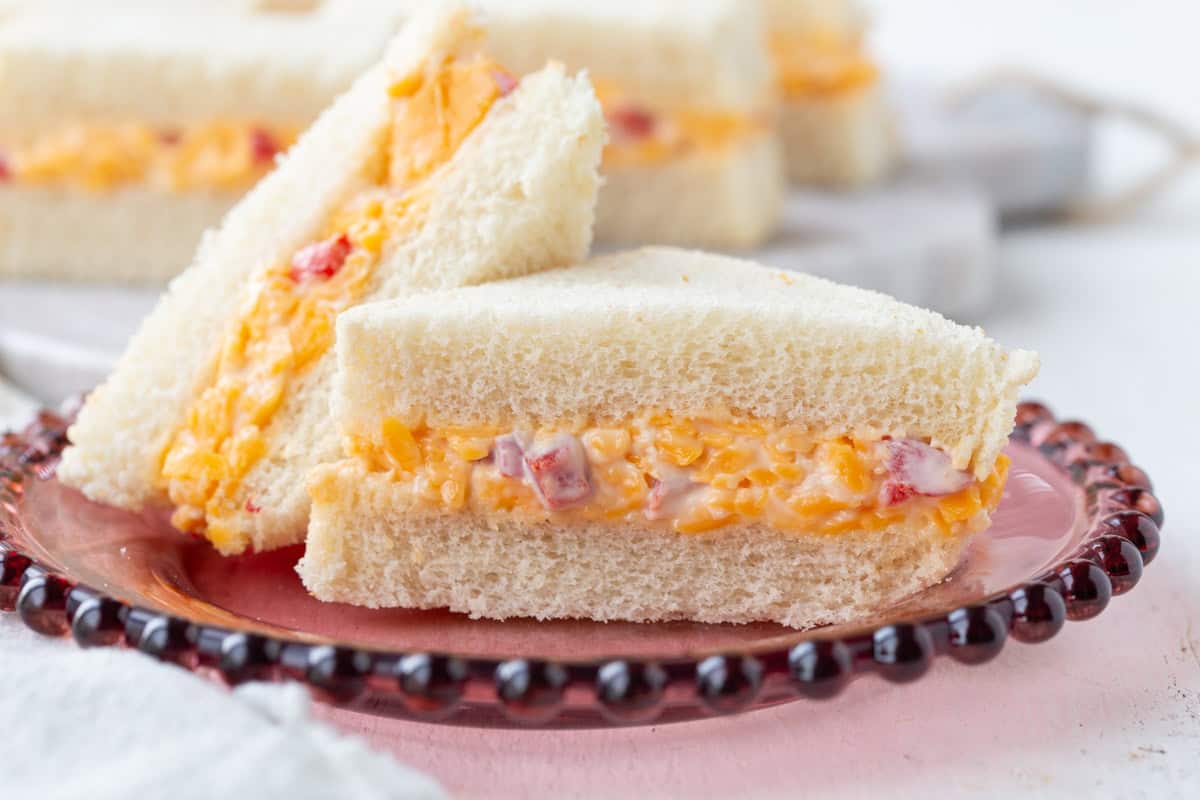 pimento cheese finger sandwiches cut into triangles on a decorative plate.