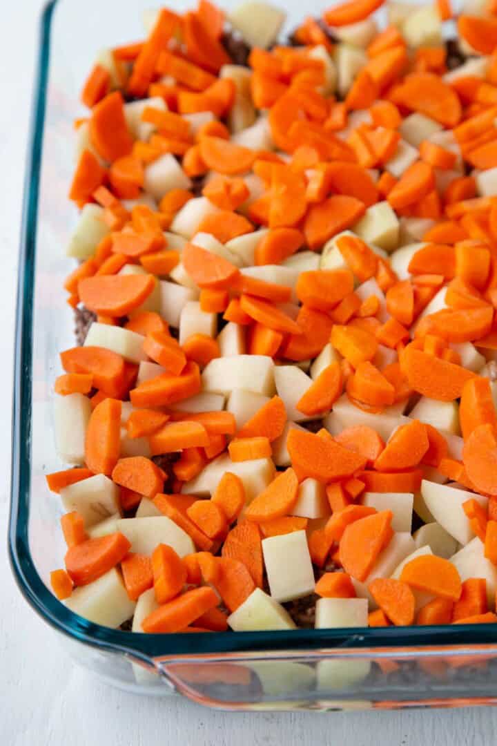 ground beef topped with potatoes and carrot pieces in a casserole dish.