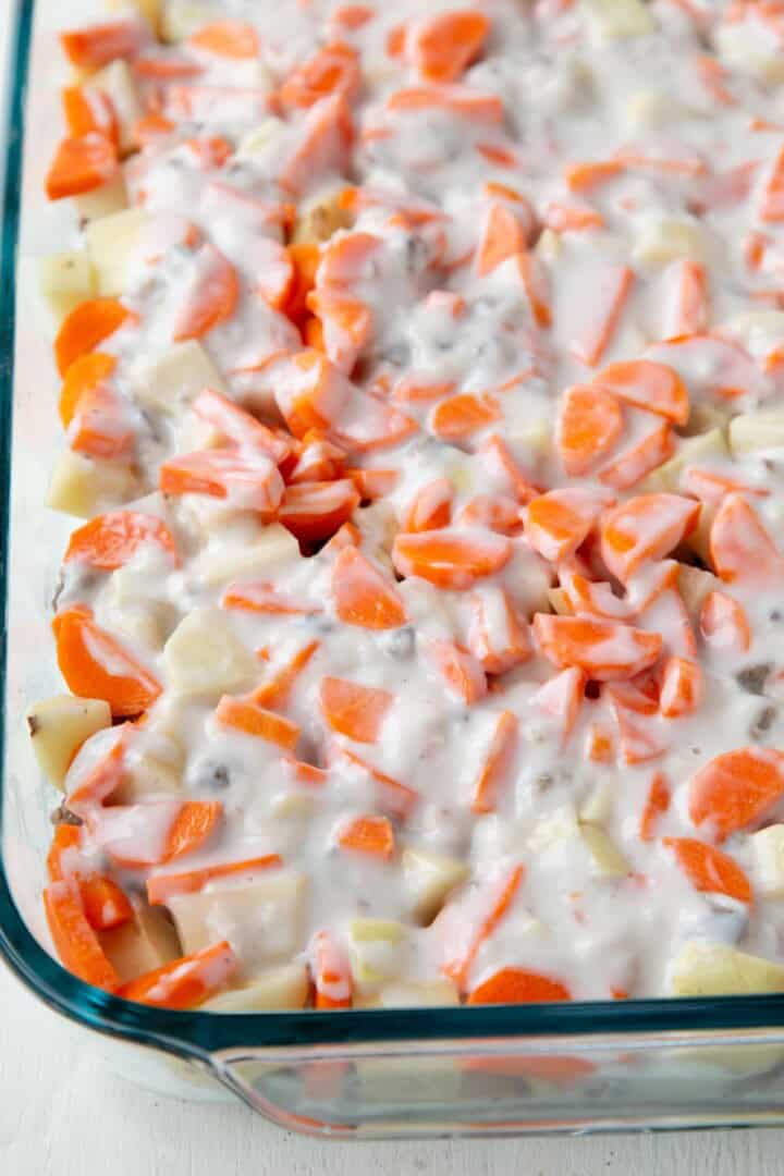 cream of mushroom soup poured over carrots and potatoes in a casserole dish.