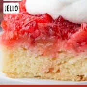 slice of rhubarb upside down cake with white cake on the bottom and a pink rhubarb topping, topped with whipped cream.