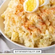 bowl of creamy potato salad topped with paprika and hard boiled egg slices.
