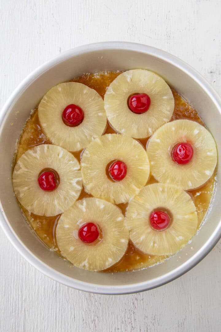 pineapple rings and maraschino cherries on top of brown sugar and butter in a cake pan.