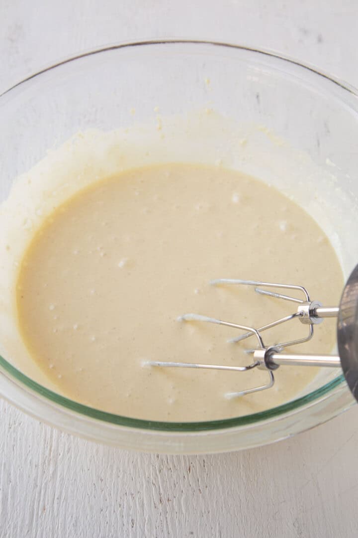 yellow cake batter with a hand mixer in a glass bowl.