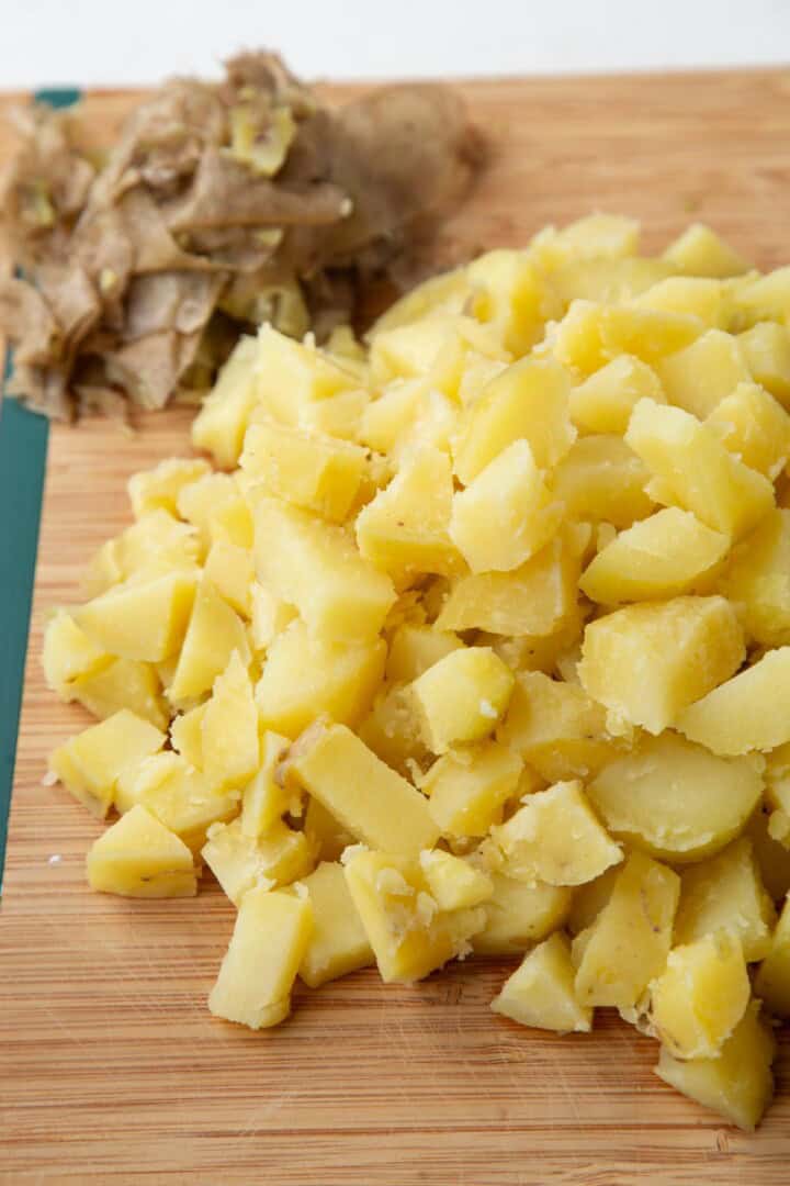 peeled and chopped cooked potatoes on a wooden cutting board.