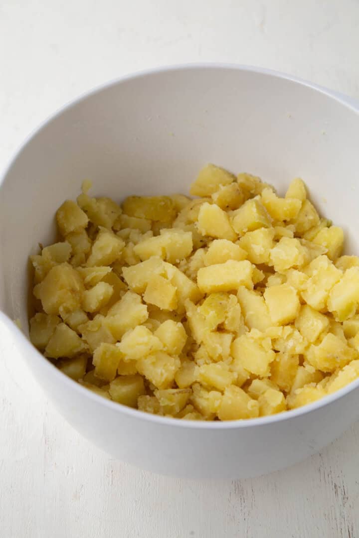peeled and chopped potatoes in a bowl with oil and vinegar.