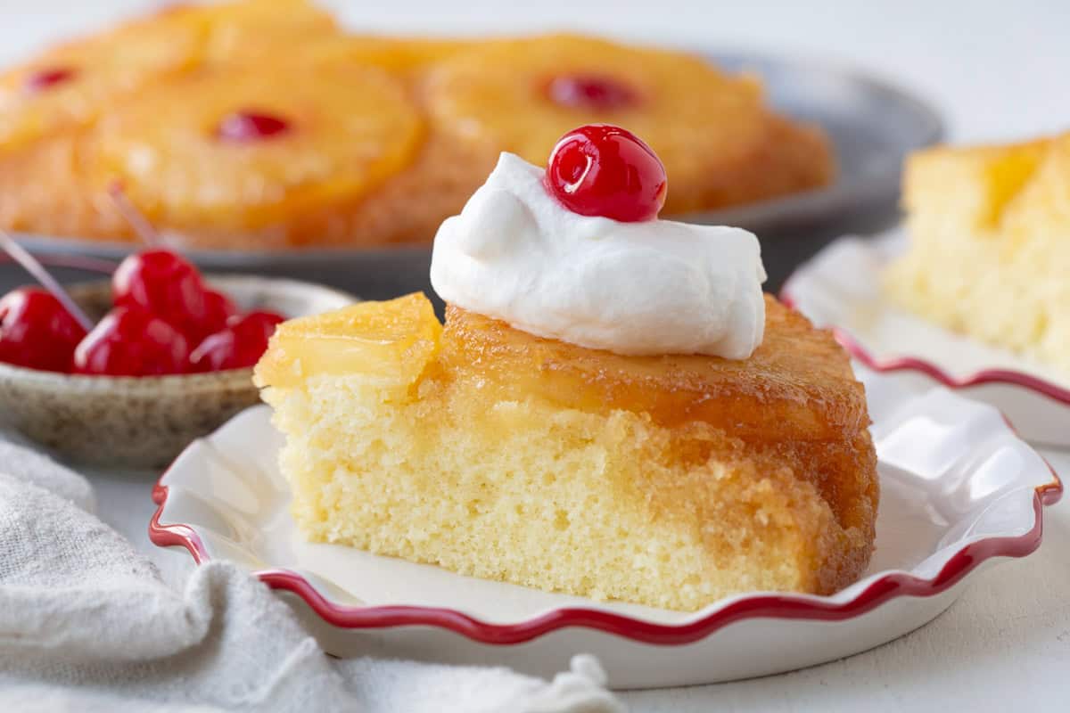 slice of pineapple upside down cake with whipped cream and a maraschino cherry on top.