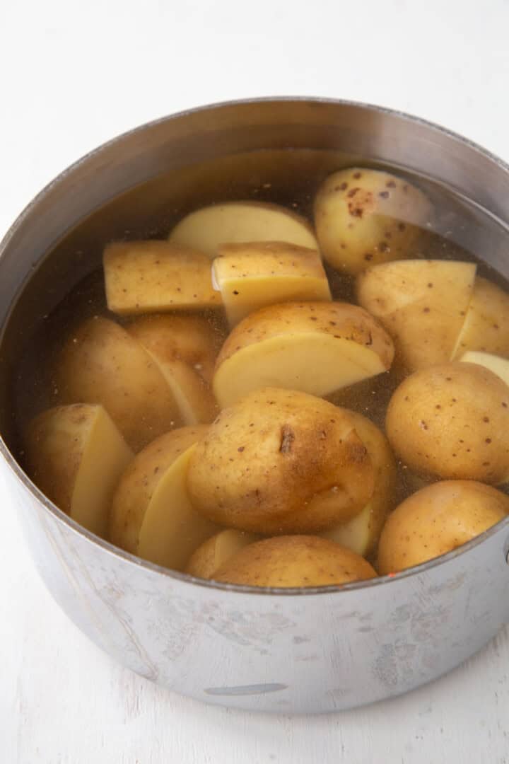 unpeeled potatoes cooking in a pan of water.