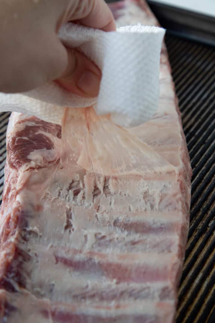 hand pulling the membrane off a rack of saint louis ribs.