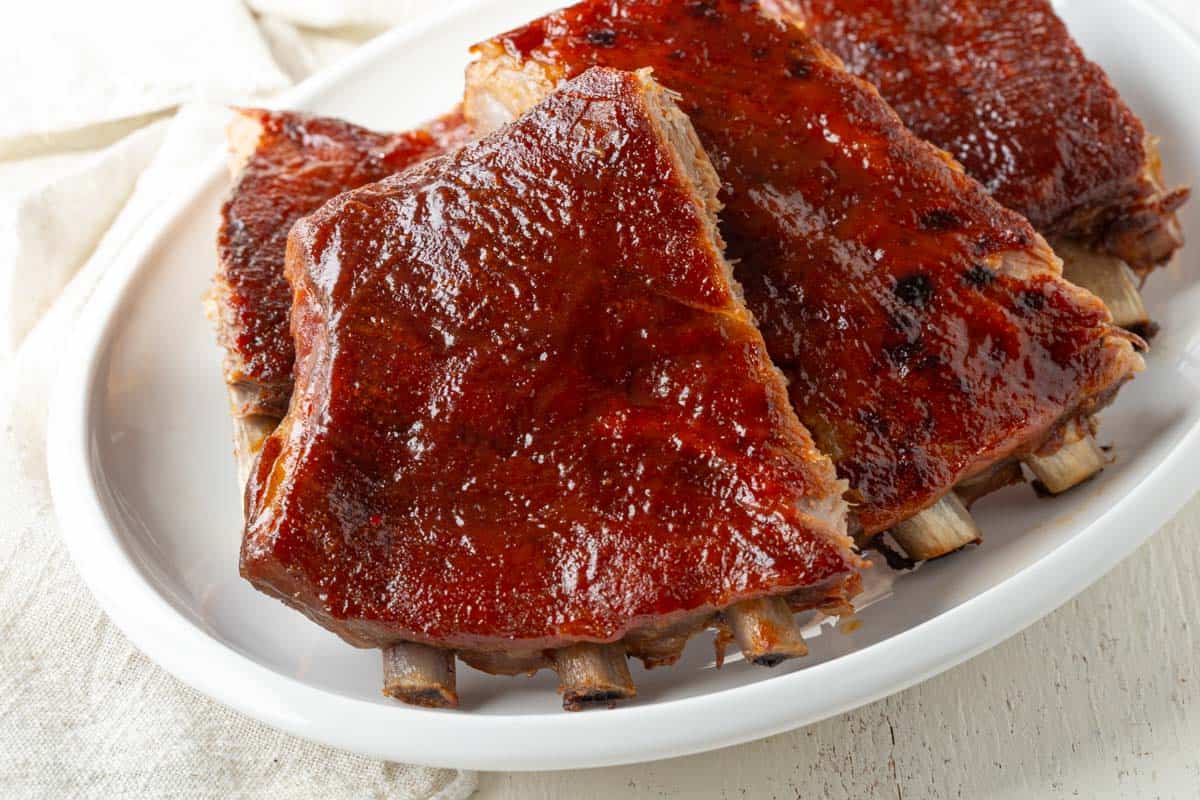 sliced ribs with bbq sauce on a white serving platter.