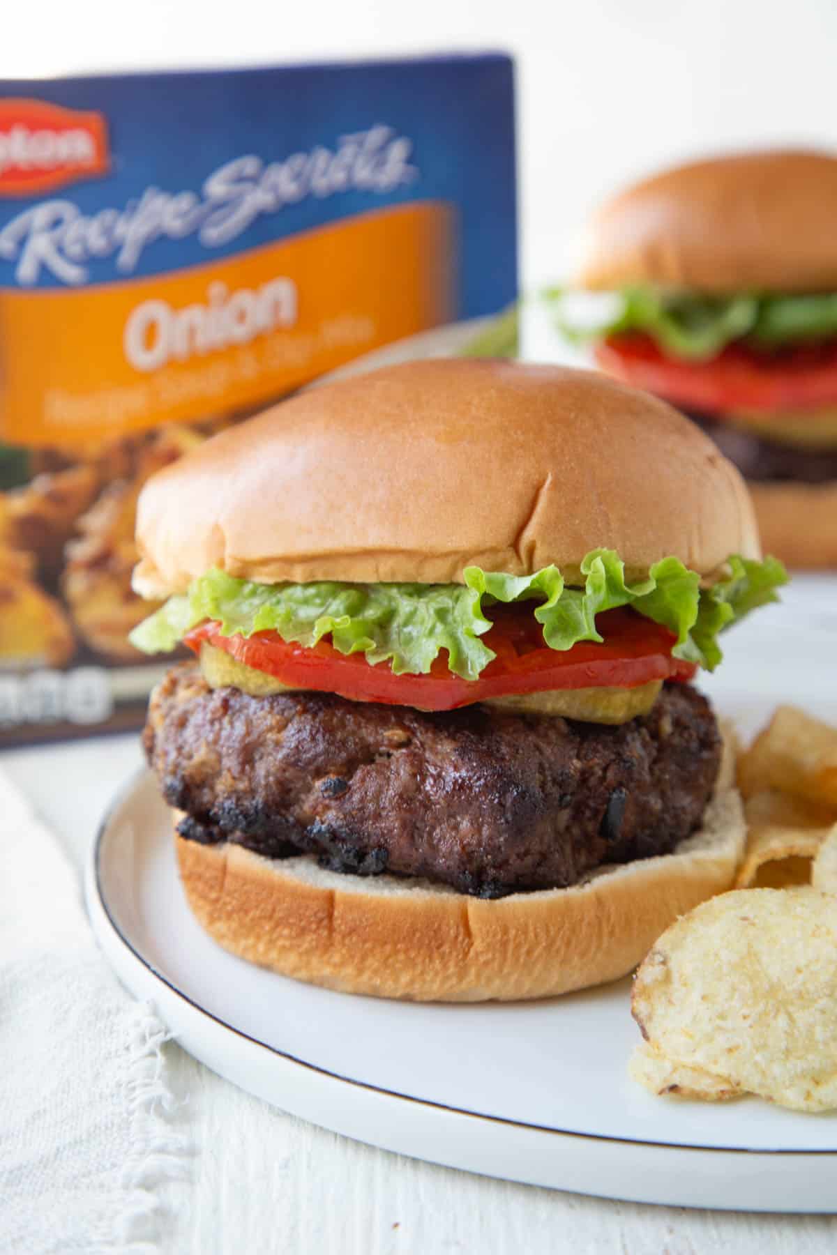 a burger on a bun with lettuce and tomato, next to a box of french onion soup mix.