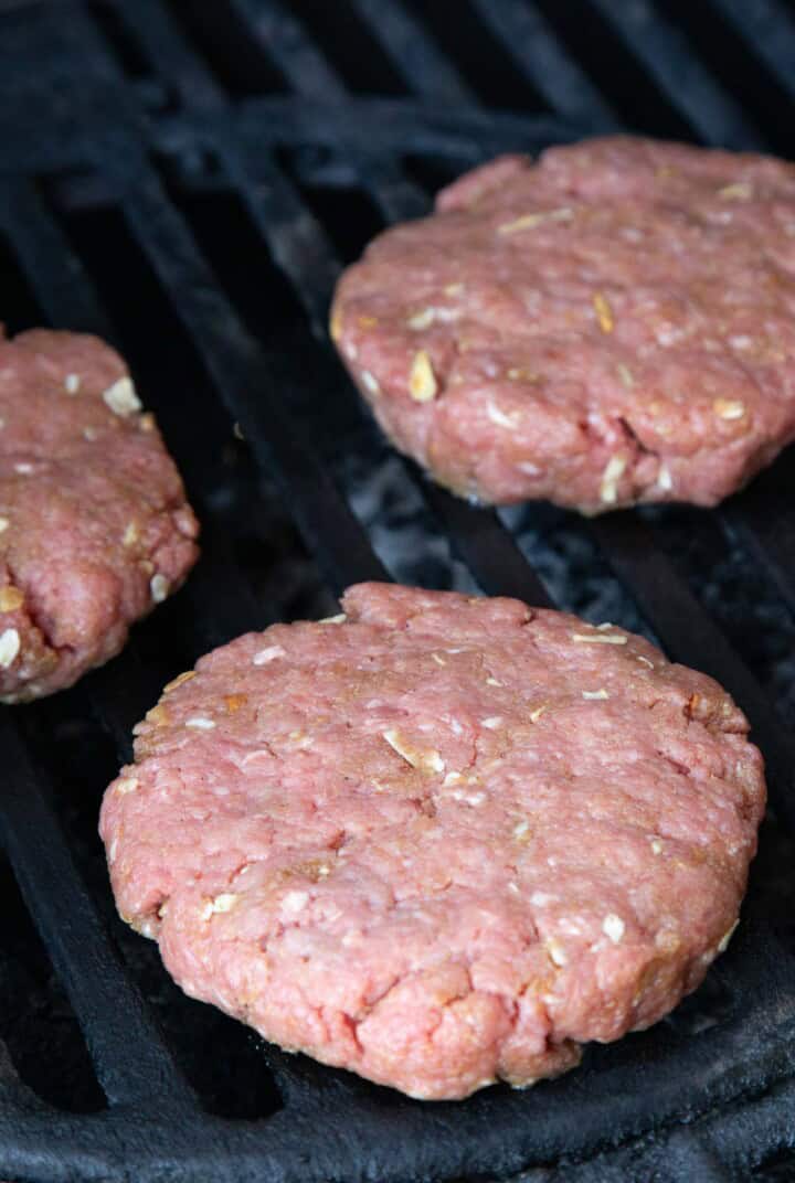 raw burger patties on a grill.