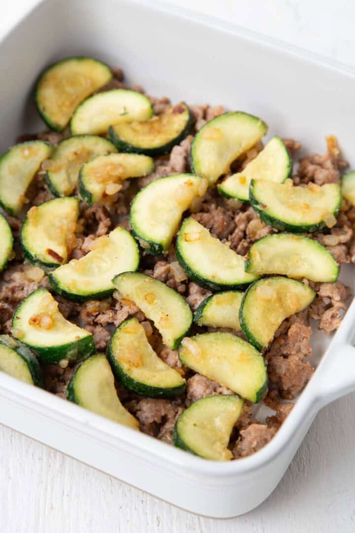sausage topped with zucchini in a casserole dish.