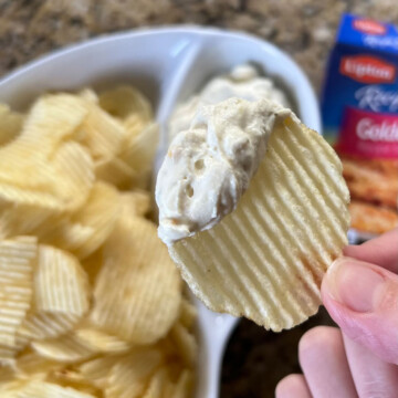 hand holding a chip topped with a dollop of creamy onion soup mix sour cream dip.