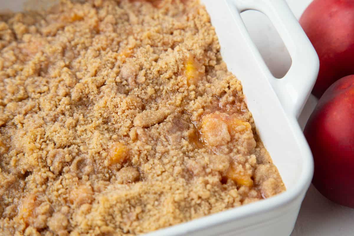 nectarine crumble in a white baking dish, next to two fresh nectarines.