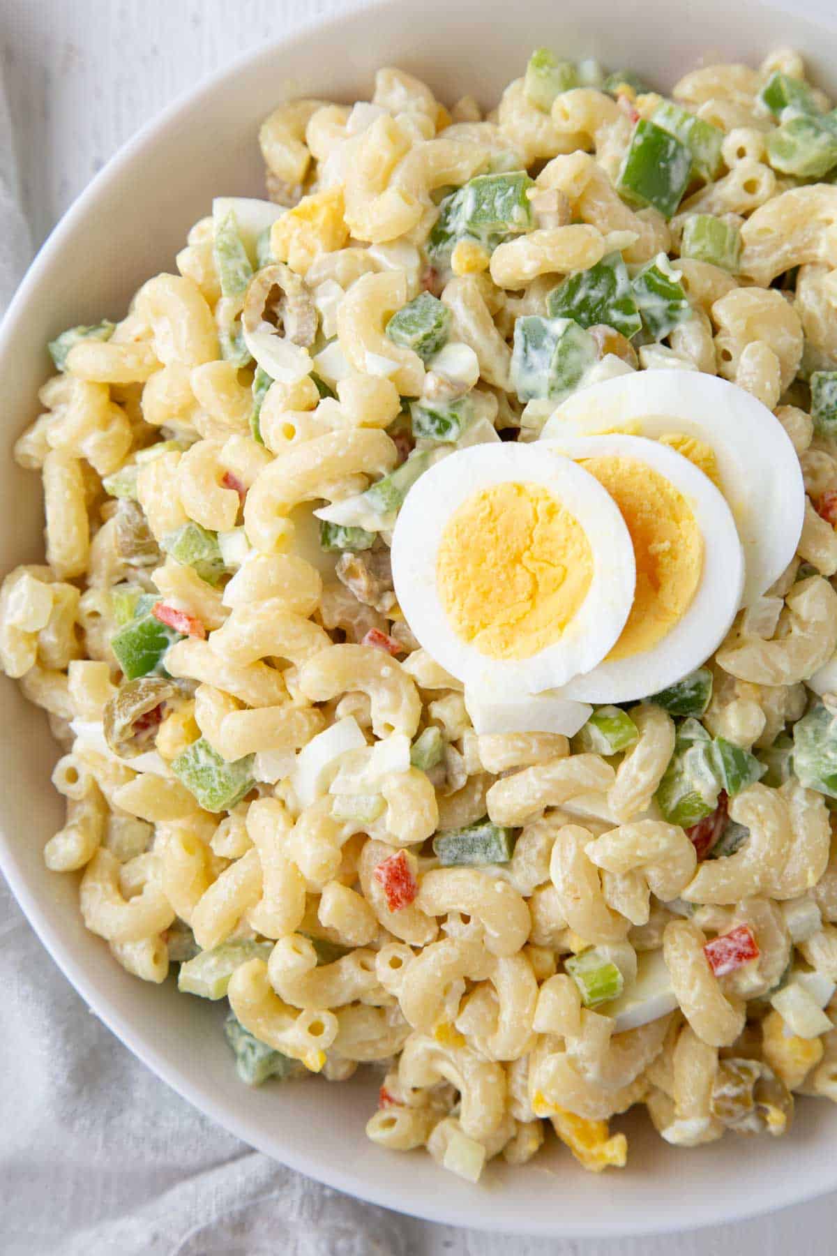 bowl of macaroni salad with olives and sliced hard boiled eggs on top.